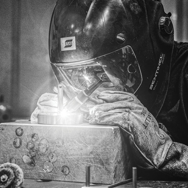 Black and white photo of a welder providing precision manufacturing services on a piece of metal.