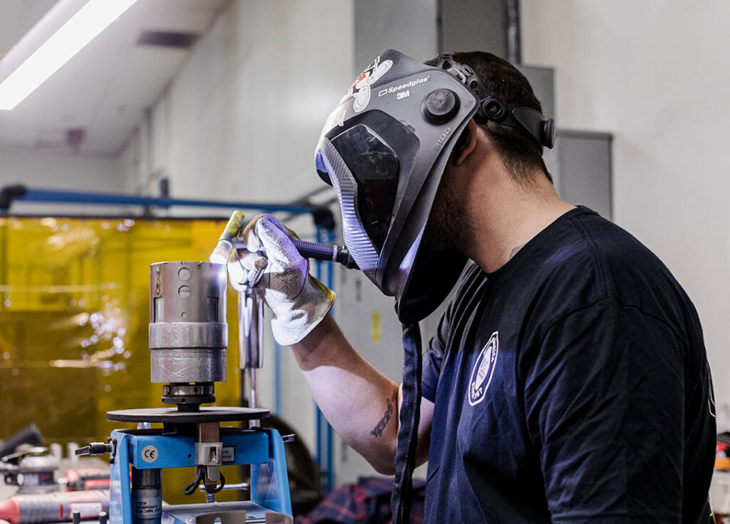 A man wearing a welding mask working on a machine, providing Precision Welding Solutions.